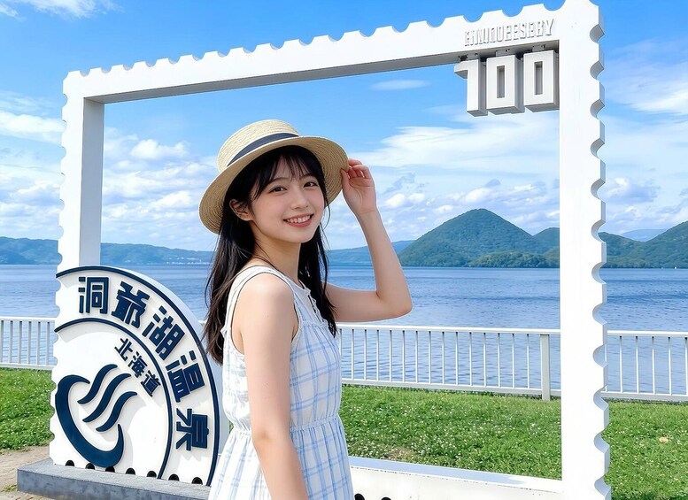 A person standing in front of a sign with Japanese characters, a white fence, and a body of water with mountains in the background. 1