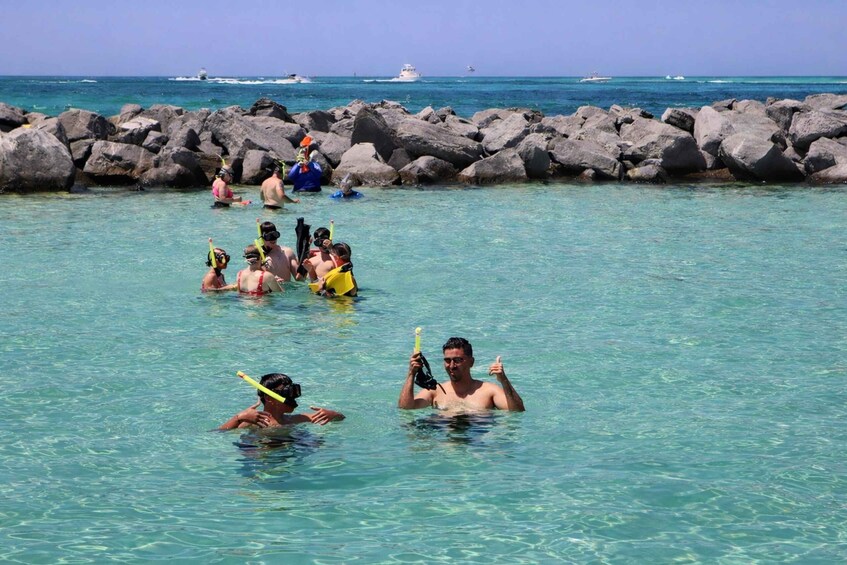 People snorkeling in clear blue water with a rocky breakwater in the background. 5