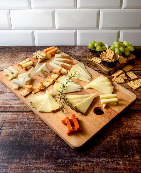 A wooden board with various cheeses, crackers, and grapes. 3
