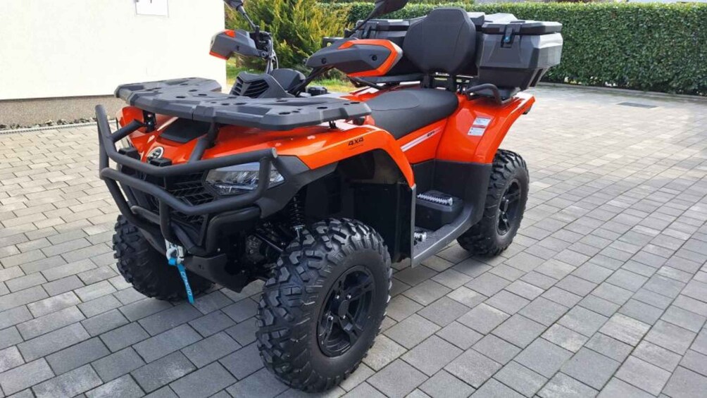 An orange ATV with large tires and a storage box on the back. 3