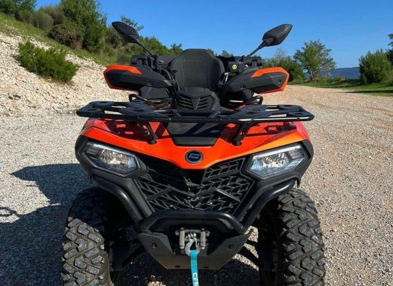 A quad bike parked on a gravel path with a clear sky and vegetation in the background. 2