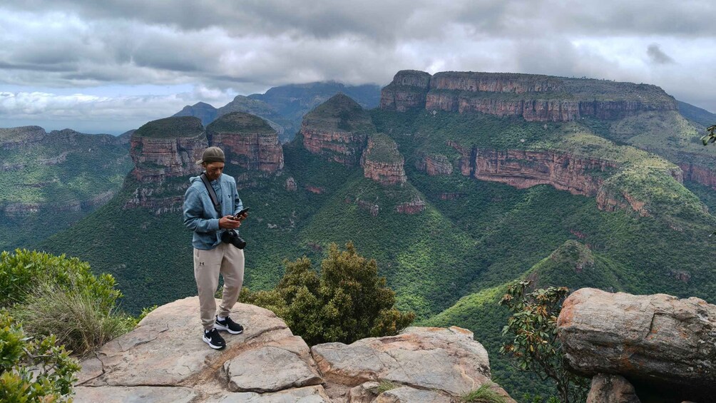 A person standing on a rocky outcrop overlooking a canyon with steep cliffs and dense greenery. 5