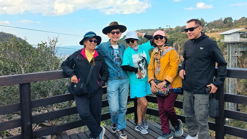 A group of people on a wooden bridge with greenery and hills in the background. 2