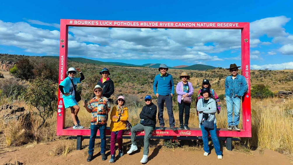 A group of people posing in front of a red sign with text about a nature reserve. 5