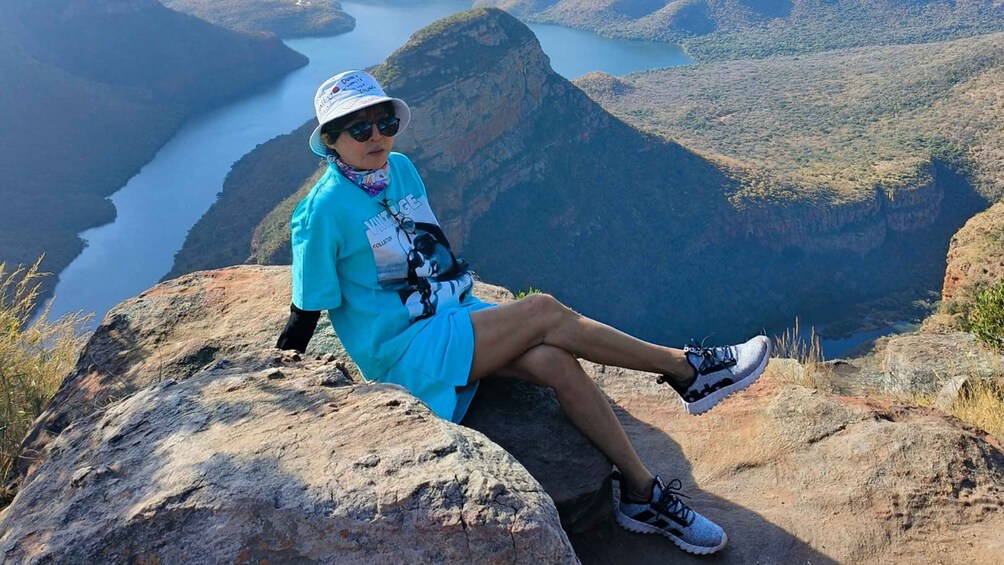 A person sitting on a rock with a scenic view of a canyon and a river. 4