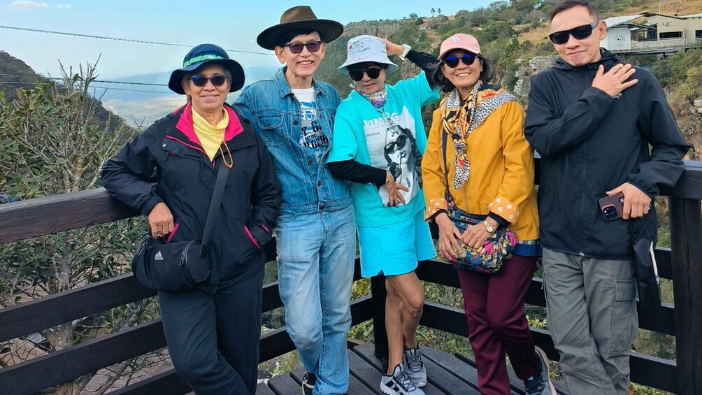 A group of people on a wooden bridge with a scenic view of hills and a clear sky. 5
