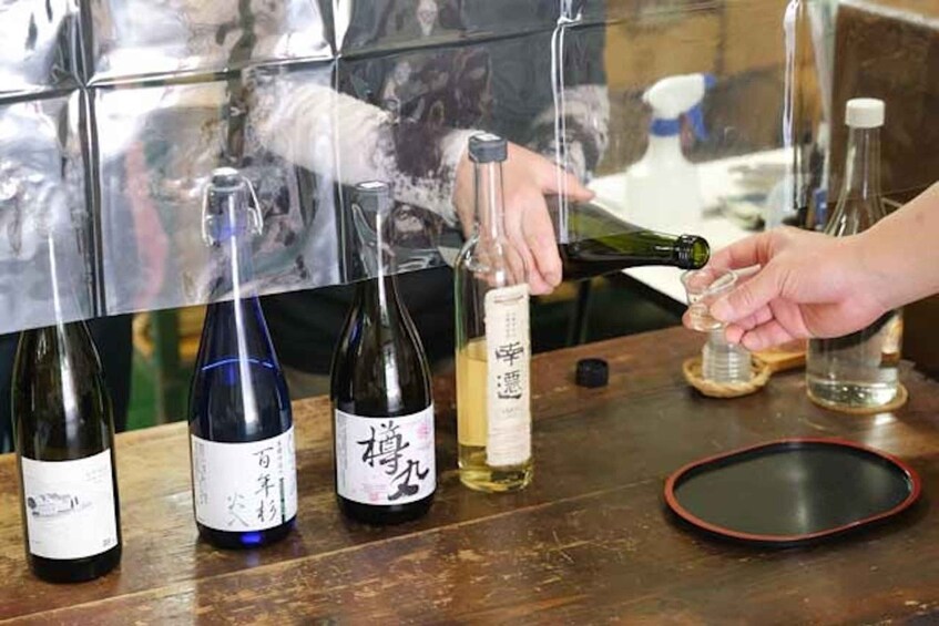A person pouring a liquid from a green bottle into a clear glass. There are other bottles and a red plate on the table. 3