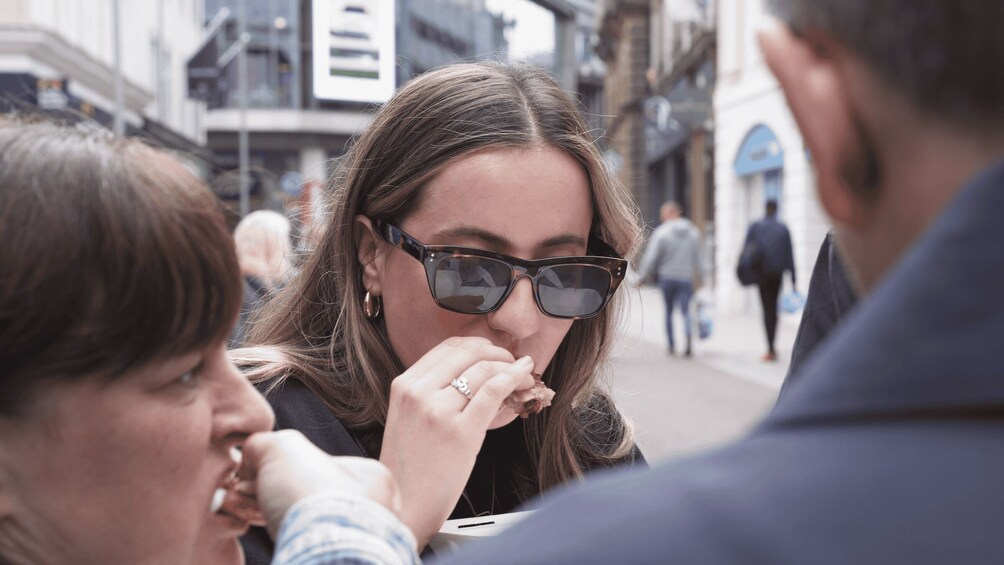 A person wearing sunglasses and a ring, with a blurred background of a city street. 1