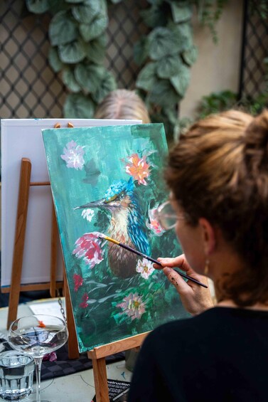 A person painting a bird with flowers on a canvas. 4