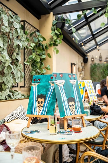 An outdoor café with tables, chairs, and art on easels. 3