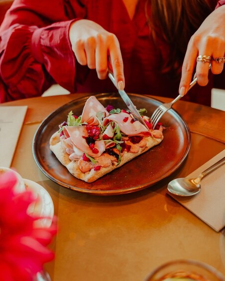 A person in a red jacket cutting a dish with a fork and knife on a brown plate. 2