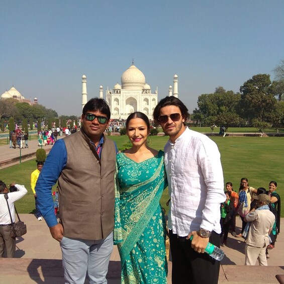 Three people standing in front of the Taj Mahal with a crowd in the background. 4