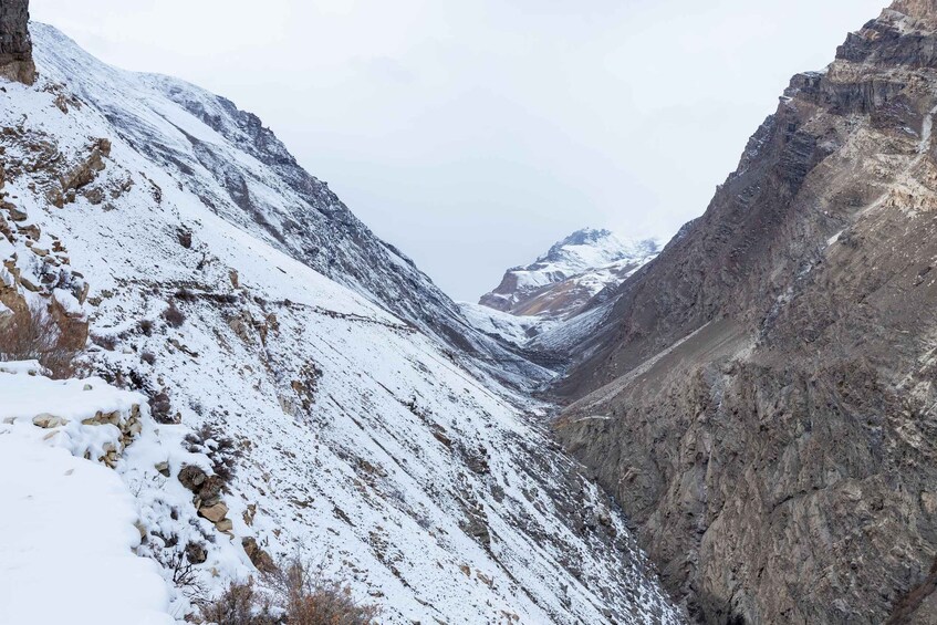 A snow-covered mountain pass with rocky terrain and a distant peak. 2