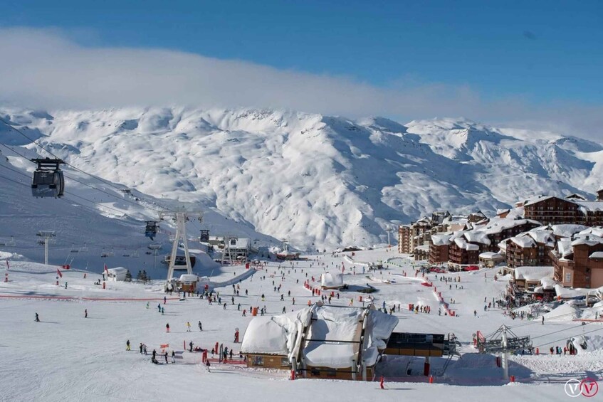 A snowy ski resort with a ski lift, buildings, and mountains in the background. 1