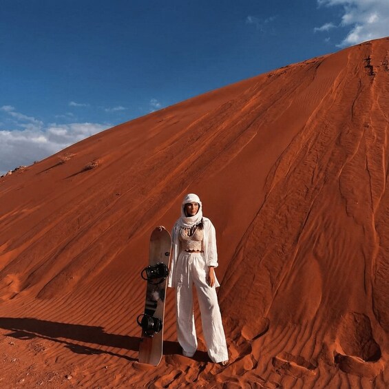 A person standing on a red sand dune with a snowboard. 4