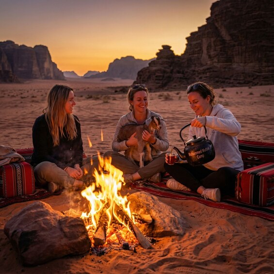 Three people sitting on a blanket around a campfire in a desert landscape with rock formations in the background. 5