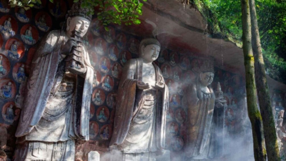 A stone Buddha statue with intricate carvings, set against a backdrop of a painted wall with multiple figures. 5
