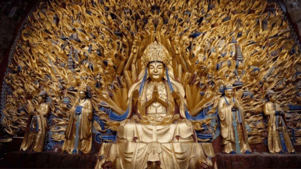 A golden statue of a seated figure with multiple arms, surrounded by smaller statues in a temple setting. 2