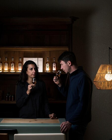 Two people tasting wine at a bar with bottles in the background. 1