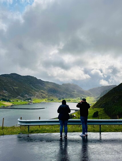 Two people standing on a wet road, overlooking a lake with mountains in the background. 5