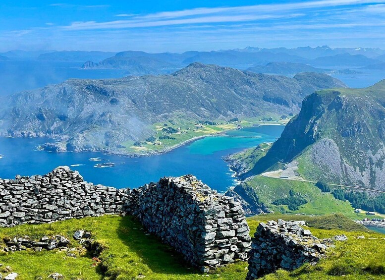 A mountainous landscape with a clear blue lake, stone ruins, and a distant view of a rugged coastline. 3
