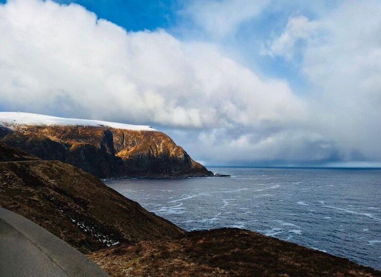 A coastal landscape with a snow-covered cliff, ocean waves, and a partly cloudy sky. 1
