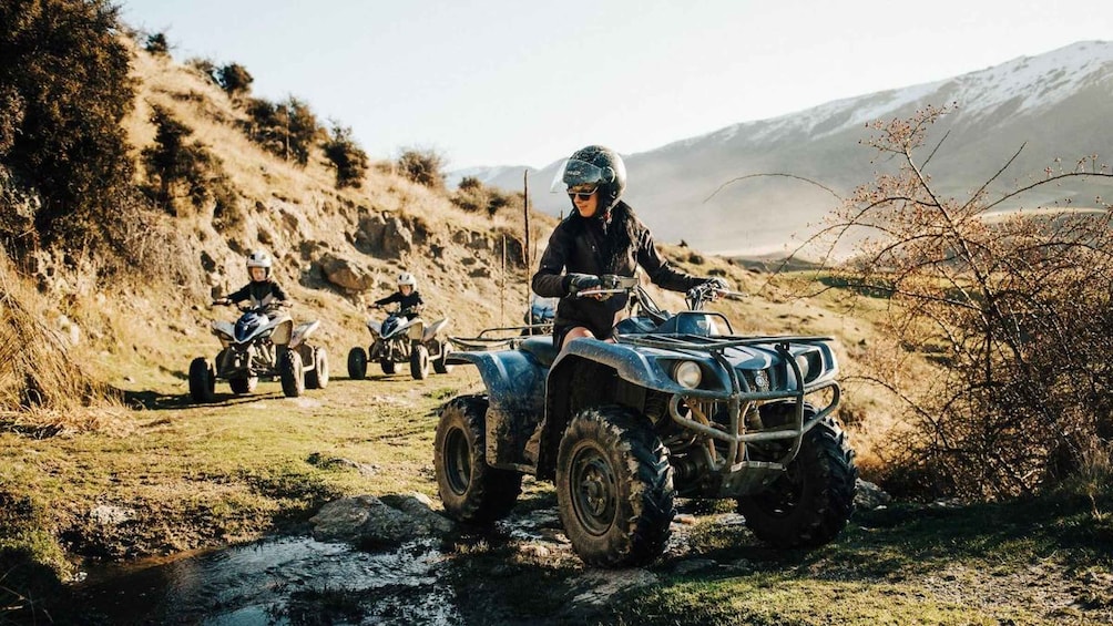 A person riding an ATV on a dirt path with a mountainous landscape in the background. 1