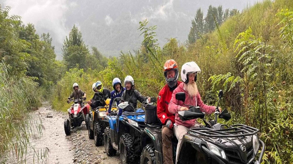 A group of people on ATVs on a muddy trail surrounded by dense vegetation. 2