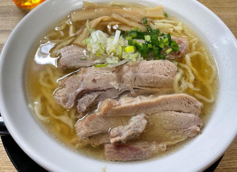 A bowl of noodle soup with sliced meat and chopped green onions. 3