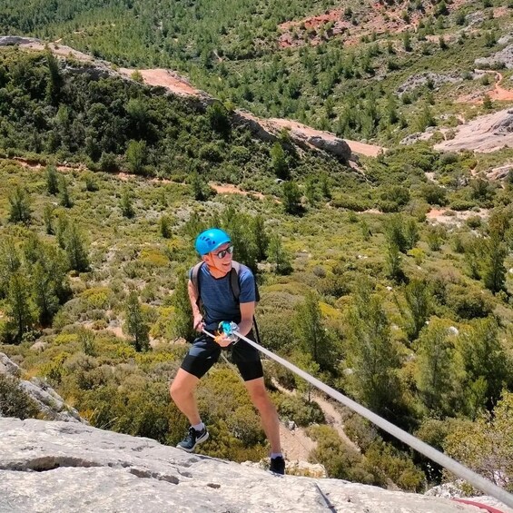A person rappelling down a rocky cliff with a rope, surrounded by a mountainous landscape with sparse vegetation. 2
