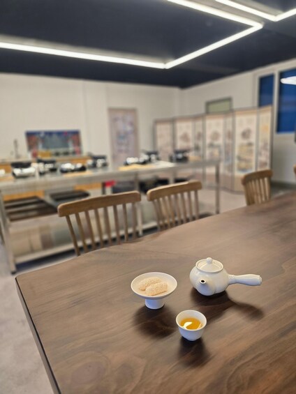 A wooden table with a white teapot, two small bowls, and a cup of tea. 5