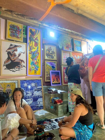 A group of people sitting and standing in a room with various framed artworks on the walls. 4