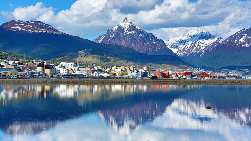 A coastal town with buildings, a calm lake, and snow-capped mountains in the background. 3