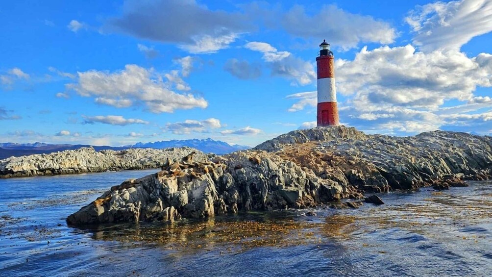 A lighthouse on a rocky outcrop with a clear blue sky and mountains in the background. 4