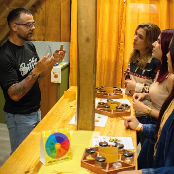 A person presenting a spinning wheel to a group of people at a wooden table with various items and a chart. 1