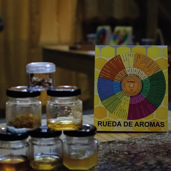 A chart titled 'Rueda de Aromas' with various labeled sections, and several glass jars with lids on a countertop. 2