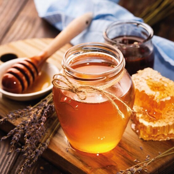 A jar of honey with a honey dipper and a honeycomb on a wooden surface. 5