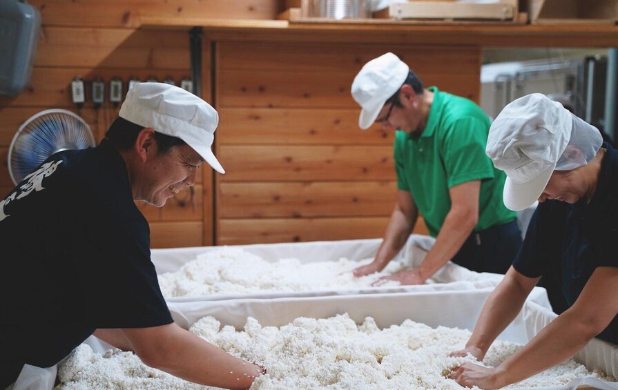 Three people wearing hats working with rice in a wooden room. 1