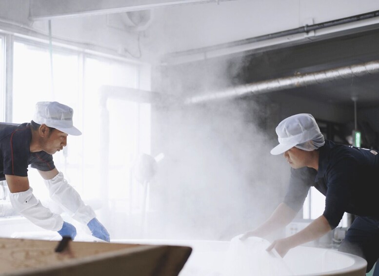 Two people in a kitchen, one wearing a white hat and white gloves, and the other in a dark shirt and white hat, working with a white object on a table. 5