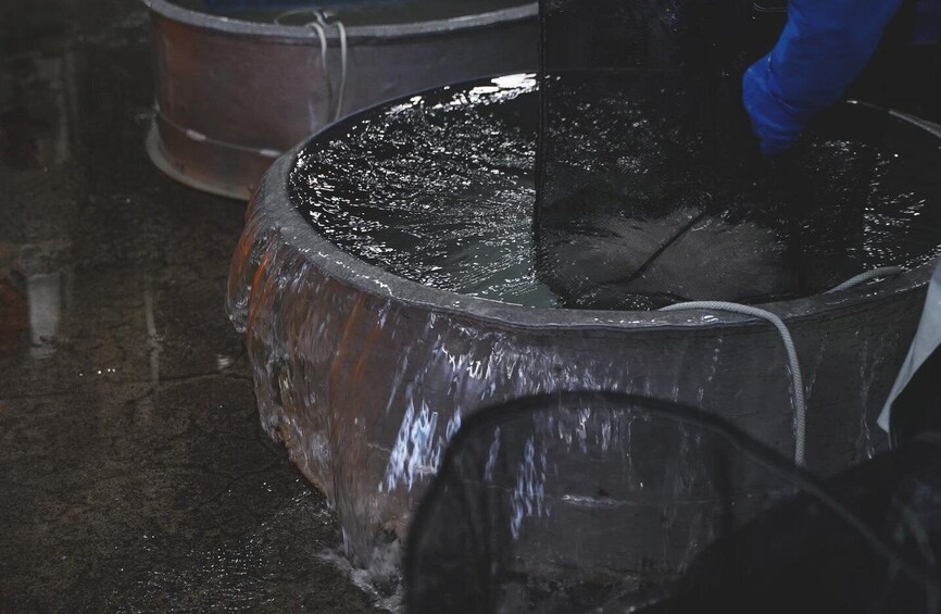 A large metal container with water, possibly for industrial use, and a person in blue gloves handling it. 4