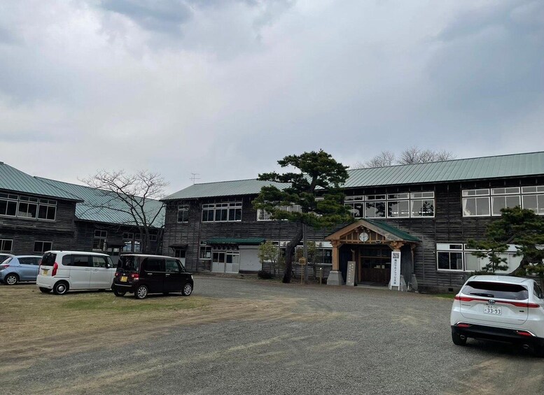 A building with a green roof, parked cars, and a tree in front. 3