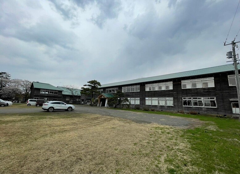 A building with a green roof, a parking lot with several cars, and a grassy area. 2