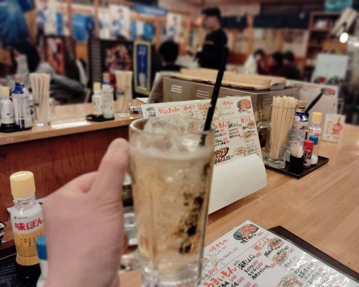 A person holding a glass with a straw, a menu, and condiments on a table in a restaurant. 5