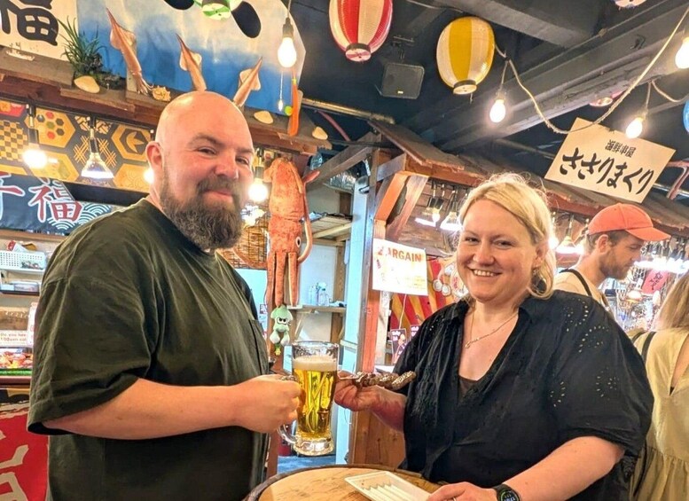 A man and a woman holding drinks in a bar with a colorful ceiling and various decorations. 1