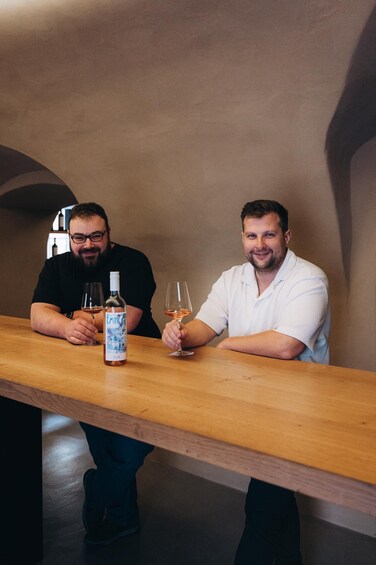 Two men sitting at a wooden table with a bottle of wine and glasses. 5