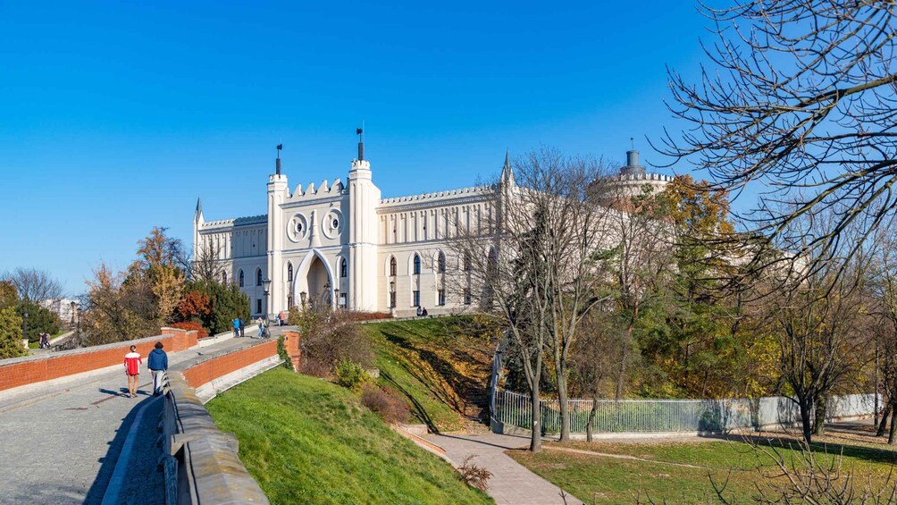 A large historic building with a clock tower, surrounded by a park with trees and a pathway. 2