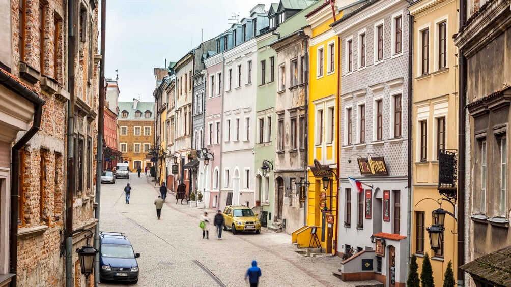A cobblestone street lined with colorful buildings, a yellow taxi, and pedestrians. 3