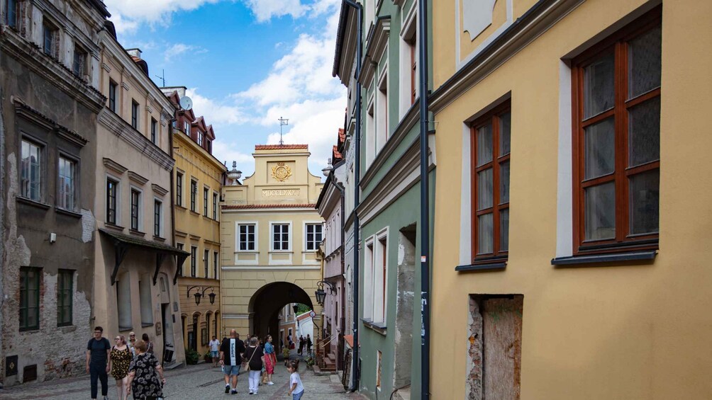 A narrow street with historic buildings, an archway, and pedestrians. 5