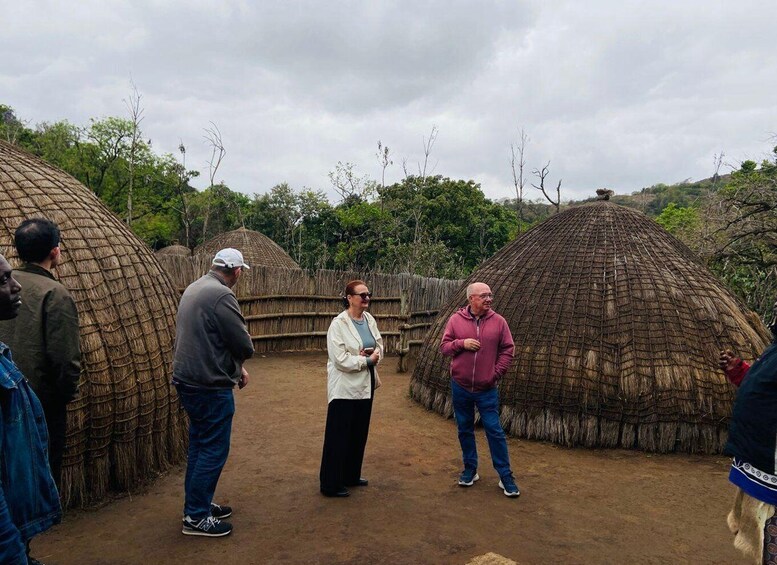 A group of people standing in front of thatched huts in a rural setting. 3