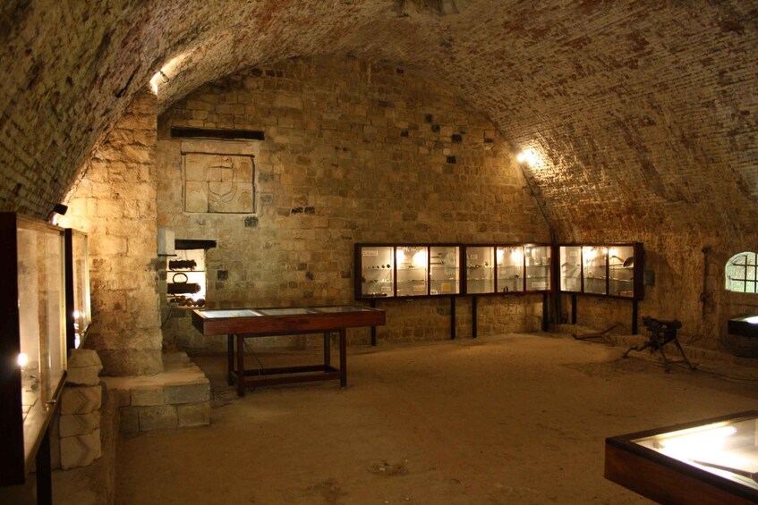 An underground room with stone walls, a wooden table, and glass display cases. 4